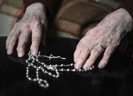 Close up of old woman praying with silver rosary with cross  in her hands at home.Sick woman calling to Godの写真素材