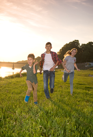 Friendship, childhood and leisure concept.  Group of happy friends playing catch-up game and running in summer park at sunset. Sunny summer dayの写真素材
