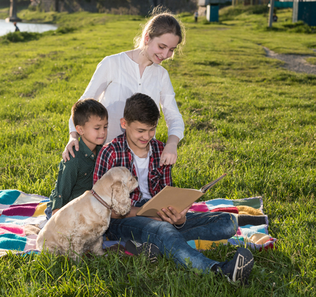 Summer, childhood, leisure concept. Children sitting on the grass and reading book in the park....