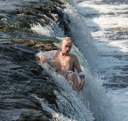 Beautiful young seminude woman in white shirt enjoying summertime in the waterfall. Enjoying and relaxing in the water. Summer sunny dayの写真素材