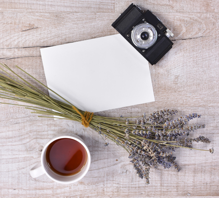 Top view of  cup of tea, lavender, vintage camera and sheet of paper on a light wooden backgroundの写真素材