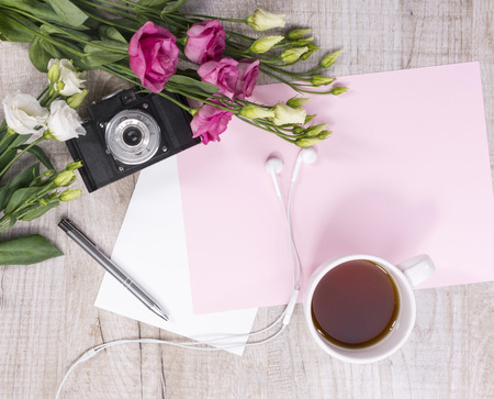 Top view of cup of tea, flowers, vintage camera, earphones, pen and sheet of paper on a light wooden background. Flat lay styleの写真素材