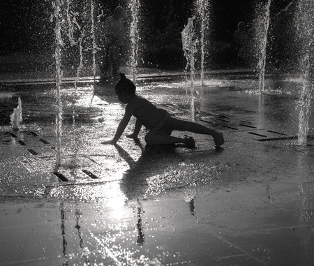 Happy girl having fun between water jets in fountain. Summer timeの写真素材
