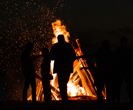 People resting near big bonfire outdoors at night