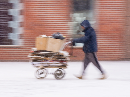 Poor man pulling a cart with cardboard in the city in snowy winter day. Intentional motion blurの写真素材