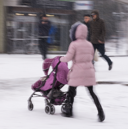 Mother walks with the child in the stroller in snowy winetr day. Intentional motion blur. Defocused imageの写真素材
