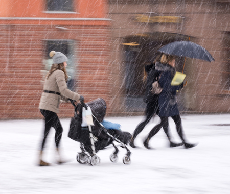 Mother walks with the child in the stroller in snowy winetr day. Intentional motion blur. Defocused imageの写真素材