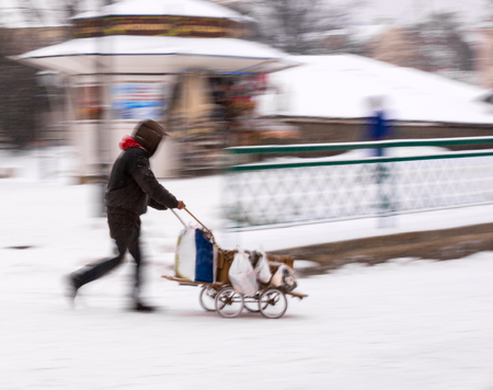 Poor man pulling a cart with cardboard in the city in snowy winter day, intentional motion blurの写真素材