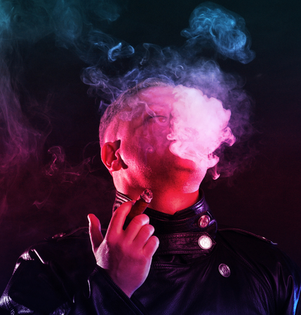 Portrait of handsome man with a cigar in leather jacket posing  in a dark roomの写真素材