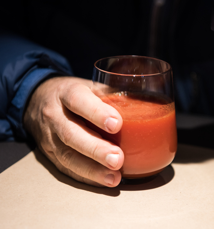 Man holding glass of tomato juice in cafeの写真素材