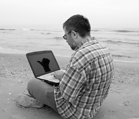 Senior businessman sitting with notebook on beachの写真素材