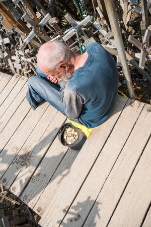 SIAULIAI, LITHUANIA - JULY 28, 2019: Hill of Crosses is a unique monument of history and religious folk art. Homeless man begging for almsのeditorial素材
