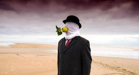 Man dressed in a black coat with closed head  and apple in his mouth posing at the beach