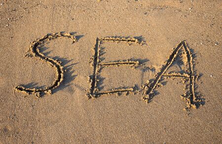 Vacation concept. Word SEA drawn on a sandy beach at sunsetの写真素材
