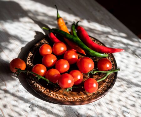 Fresh cherry tomatoes and  chilly pepper in a clay plate on a wooden backgroundの写真素材