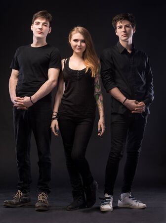 Love triangle. Young woman posing with two young man on a dark background in studio