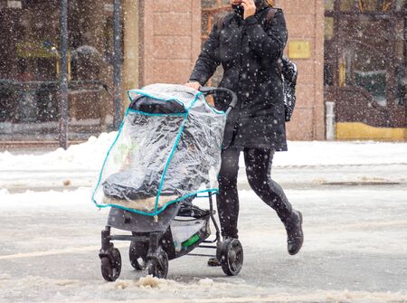 Mother walks with the child in the stroller in snowy winter day. Intentional motion blur. Defocused...