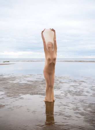 Nude model posing in stocking in the sea at the beach. Sexy woman outdoorsの写真素材