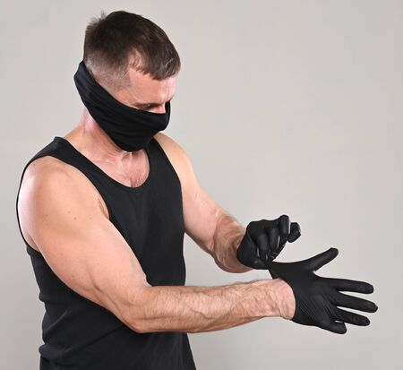 Man in black mask putting on protective gloves over gray background