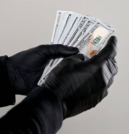 Finances concept. Man in black gloves holding pack of dollars  over gray backgroundの写真素材