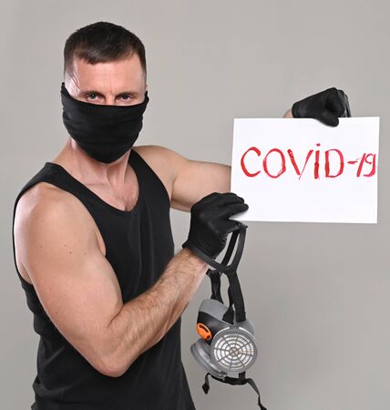Healthcare and medical concept. Man in mask holding respirator and banner with the inscription Covid-19  over gray backgroundの写真素材
