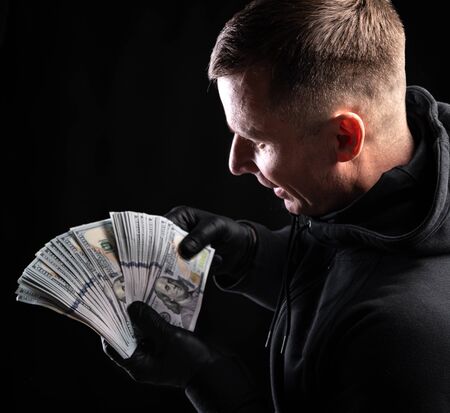 Business and finances concept. Happy smiling man in black hoody with american dollar money over black backgroundの写真素材