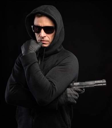 Man in black hoody with a gun posing over black backgroundの写真素材