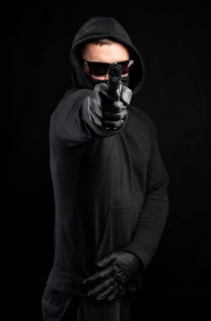 Man in black hoody with a gun posing over black backgroundの写真素材