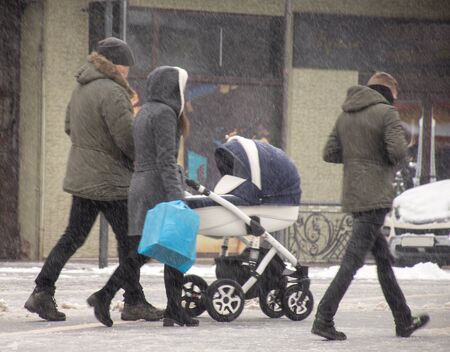 Family walking with the child in the stroller in snowy winter day. Intentional motion blur....