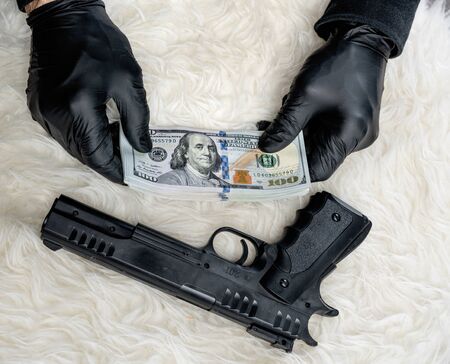Close-up view of gun and dollars in hands of robber in gloves
