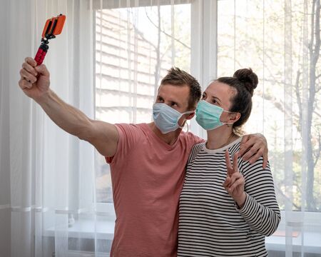 Couple in disposable masks taking selfie at home. Social distancingの写真素材
