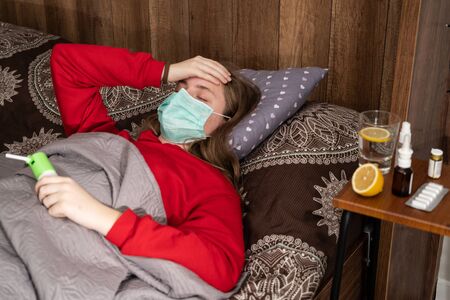 Healthcare and medical concept. Sick teen girl in mask lying in bed at homeの写真素材