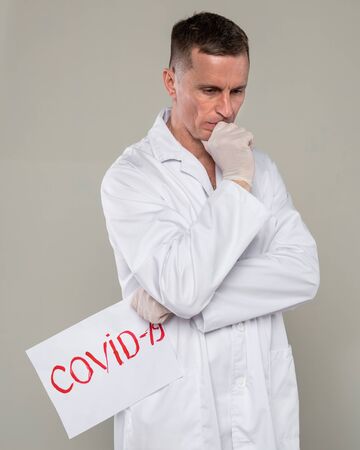 Healthcare and medical concept. Sad male doctor holding COVID-19 sign over gray backgroundの写真素材