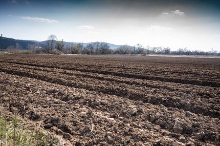 Ploughed field under blue cloudy sky in sunny early spring day