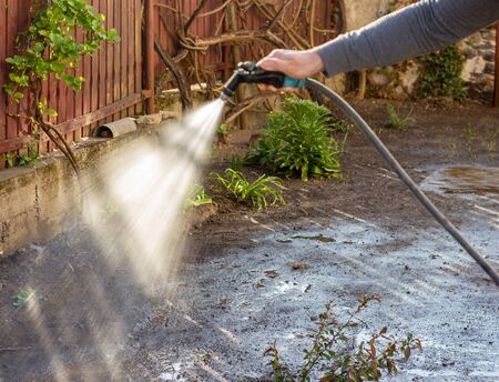 Man watering backyard lawn using hosepipe in sunny dayの写真素材