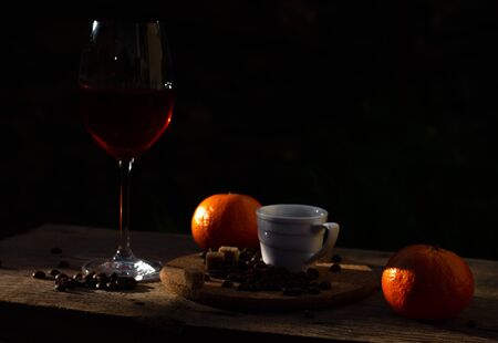 Still life with glass of red wine, coffee cup, beans and tangerines in the sun outdoorsの写真素材