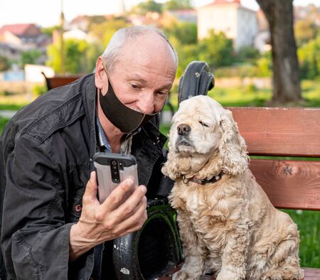 Senior man in protective mask with american cocker spaniel in the parkの写真素材