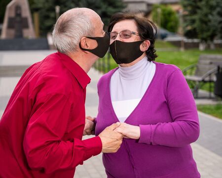 Healthcare concept. Senior couple in protective face masks kissing in the parkの写真素材