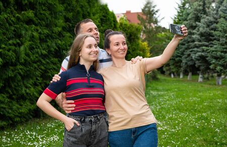 Family, leisure and technology concept. Happy mother, father and daughter taking selfie picture by smartphone in the parkの写真素材