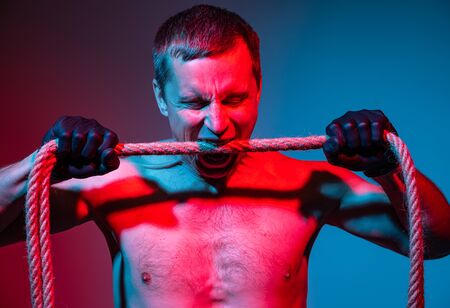 Studio image of a man in gloves bites a rope の写真素材