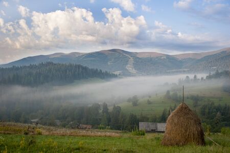 Summer landscape of rural valley. Hay stack on a green meadow in the mountains in the morningの写真素材