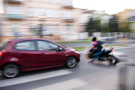 Dangerous city traffic situation with a motorcyclist and a car in motion blur. Defocused imageの写真素材