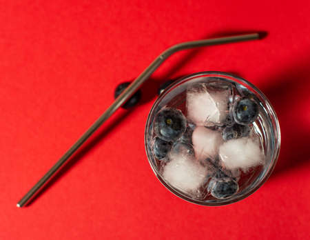 Summer refreshment drinks. Blueberry lemonade with ice cubes and metal straw on a red background