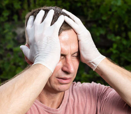 Healthcare, pain, stress concept. Sick man in protective gloves. Man suffering from headache...