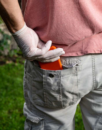 Healthcare concept.  Man in protective gloves gets out the phone from the pocket outdoorsの写真素材