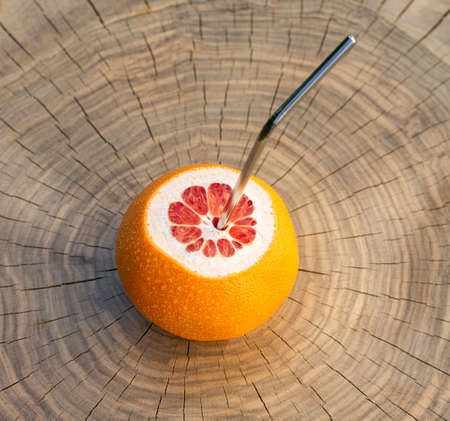 Natural fresh fruit juice concept. Red Grapefruit with metal straw on a wooden tableの写真素材