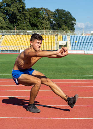 UZHHOROD, UKRAINE - SEPTEMBER 5, 2020:  Teen runner  getting ready to run doing warm-up leg stretch exercises. Male athlete stretching muscles before going running in stadium in Uzhhorod, Ukraineのeditorial素材