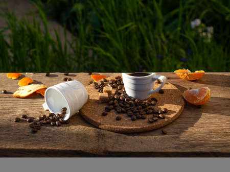 Still life with coffee cups, beans and tangerines in sun rays on a wooden table