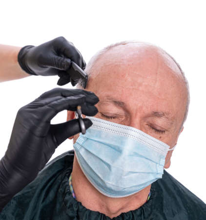 Closeup image of senior man in protective face mask  in barber shop.Barber cutting hair with...