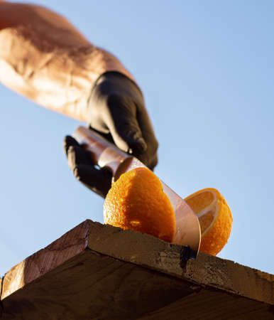 Man cutting fresh orange into two parts by knife against blue sky